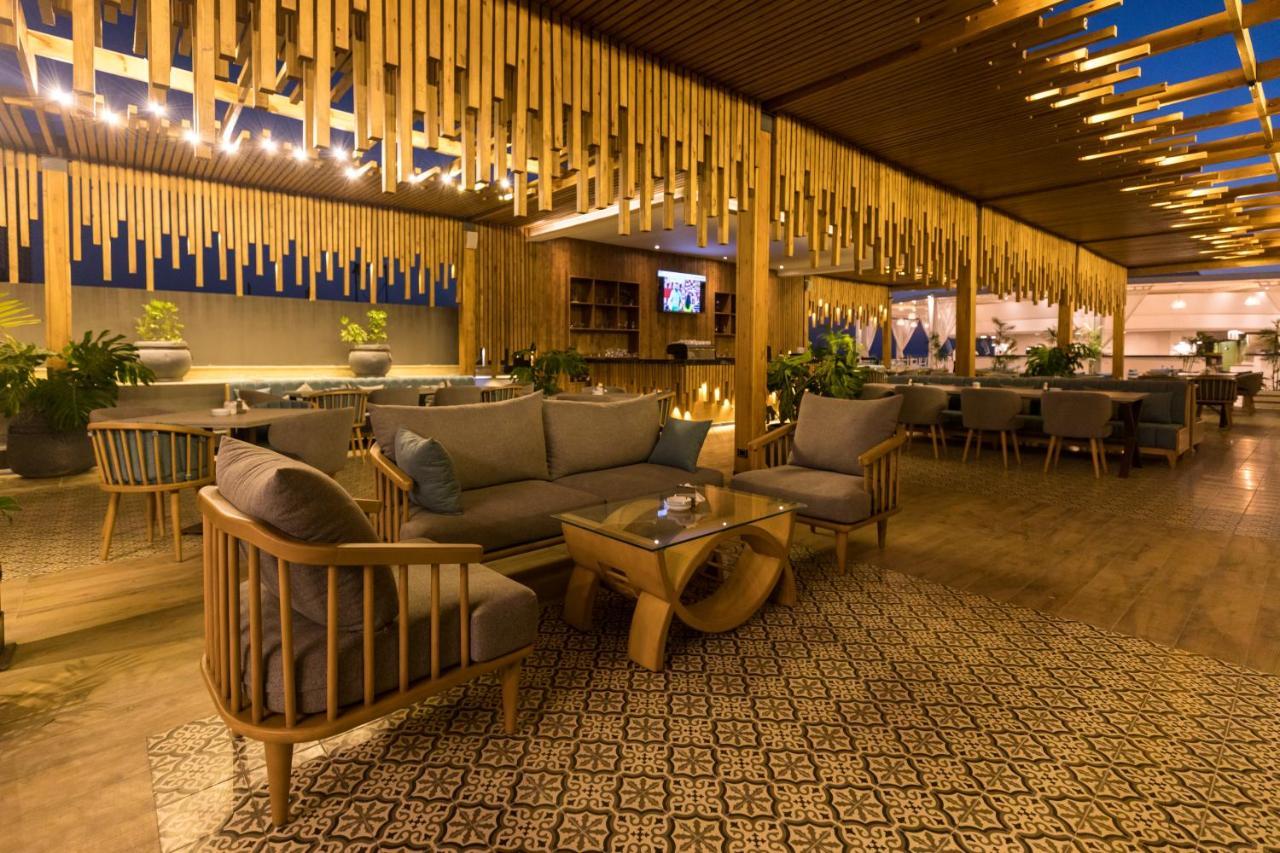 Sunrise Alex Avenue Hotel Αλεξάνδρεια Εξωτερικό φωτογραφία The photo depicts a stylish and modern lounge or restaurant interior. It features wooden furniture, including a sofa and armchairs, arranged around a central coffee table. The space is characterized by warm lighting and decorative elements, such as h
