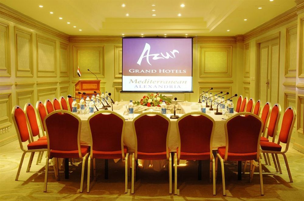 Sunrise Alex Avenue Hotel Αλεξάνδρεια Εξωτερικό φωτογραφία The photo shows a conference room set up for a meeting or event. There is a large oval table surrounded by red chairs, and the table is equipped with microphones and bottles of water. In the background, there is a projector screen displaying the logo