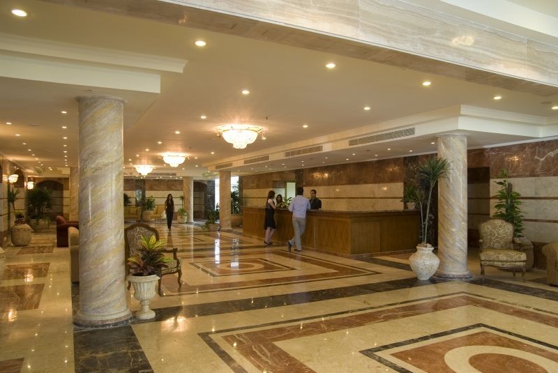 Sunrise Alex Avenue Hotel Αλεξάνδρεια Εξωτερικό φωτογραφία The photo shows the interior of a spacious lobby, likely in a hotel. There are marble floors with intricate patterns, elegant lighting fixtures, and tall pillars. In the center, there is a reception desk where staff members are attending to guests. S
